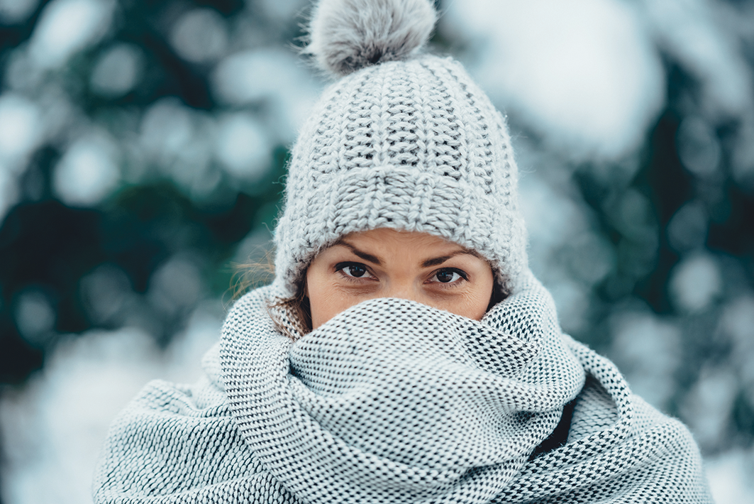 Eine Frau ist im Schnee mit einem dicken grauen Schal und einer grauen Wollmütze.