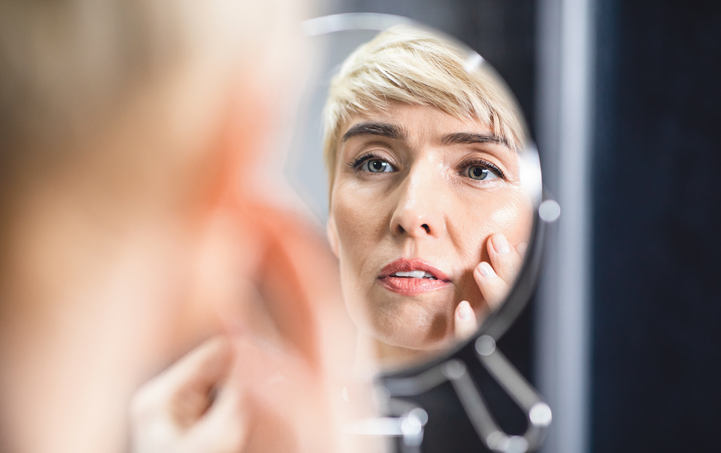 Eine Frau schaut sich ihr Gesicht in einem Spiegel an.